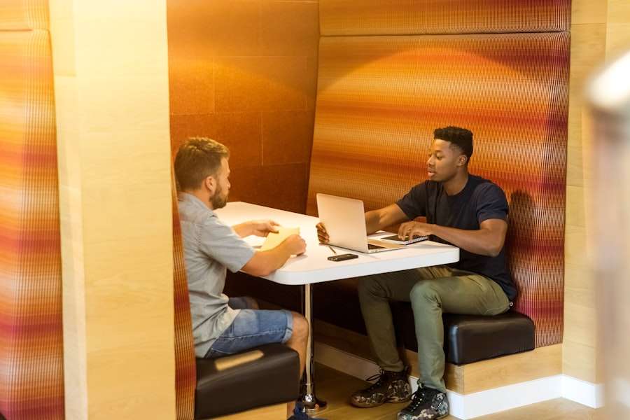 SEO Hannover - Zwei Personen sitzen an einem kleinen weißen Tisch in einer modernen, halb geschlossenen Kabine. Eine Person benutzt einen Laptop, während die andere scheinbar zuhört. Die Wände sind mit strukturierten, gestreiften Paneelen in warmen Tönen bedeckt. Local SEO Agentur Hannover.
