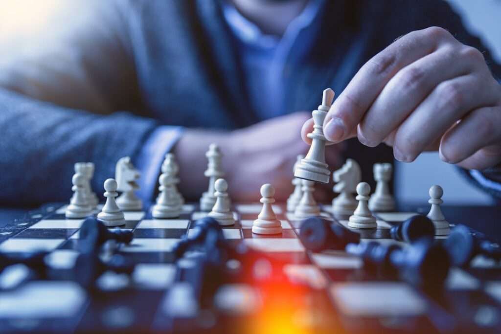 SEO Hannover - Eine Person im Anzug bewegt einen weißen Schachkönig auf einem Schachbrett, während um ihn herum andere Figuren sichtbar sind. Der Fokus liegt auf dem laufenden Schachspiel mit unscharfem Hintergrund. Local SEO Agentur Hannover.
