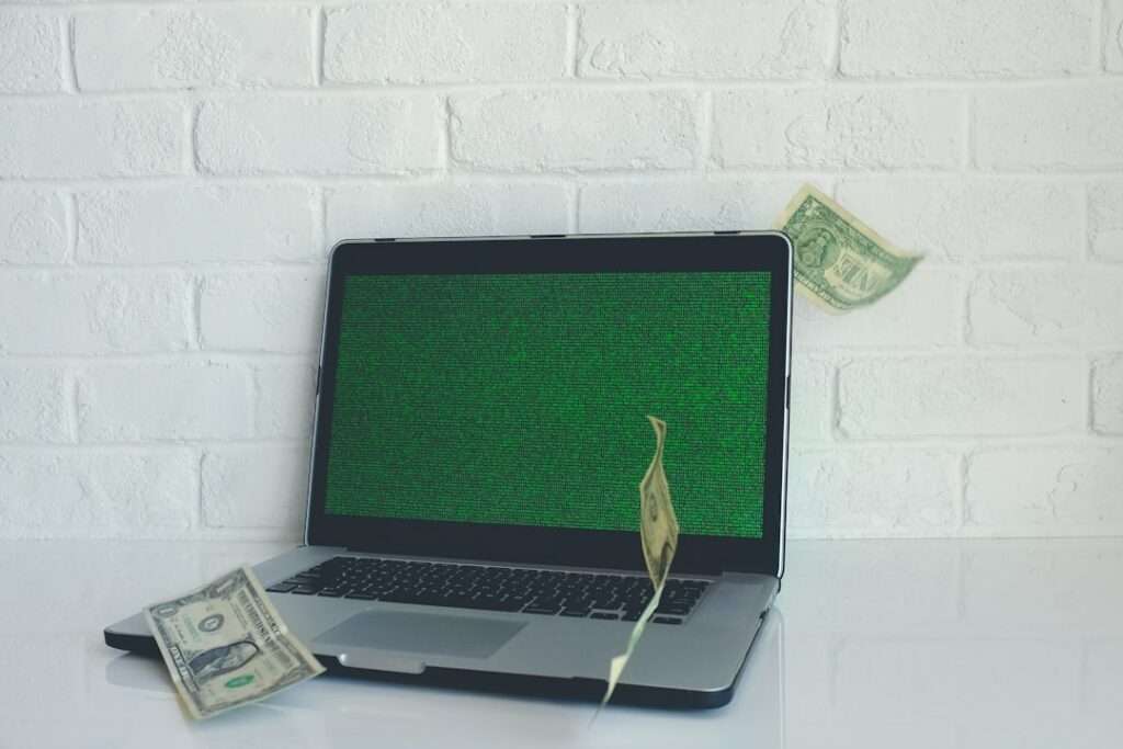 Suchmaschinenoptimierung Hannover - Ein aufgeklappter Laptop mit einem grünen matrixartigen Bildschirm steht auf einer weißen Fläche vor einer weißen Backsteinwand, um ihn herum schweben Dollarscheine. Die Szene fängt die Essenz der digitalen Kompetenz von SEO Hannover ein. Local SEO Agentur Hannover.