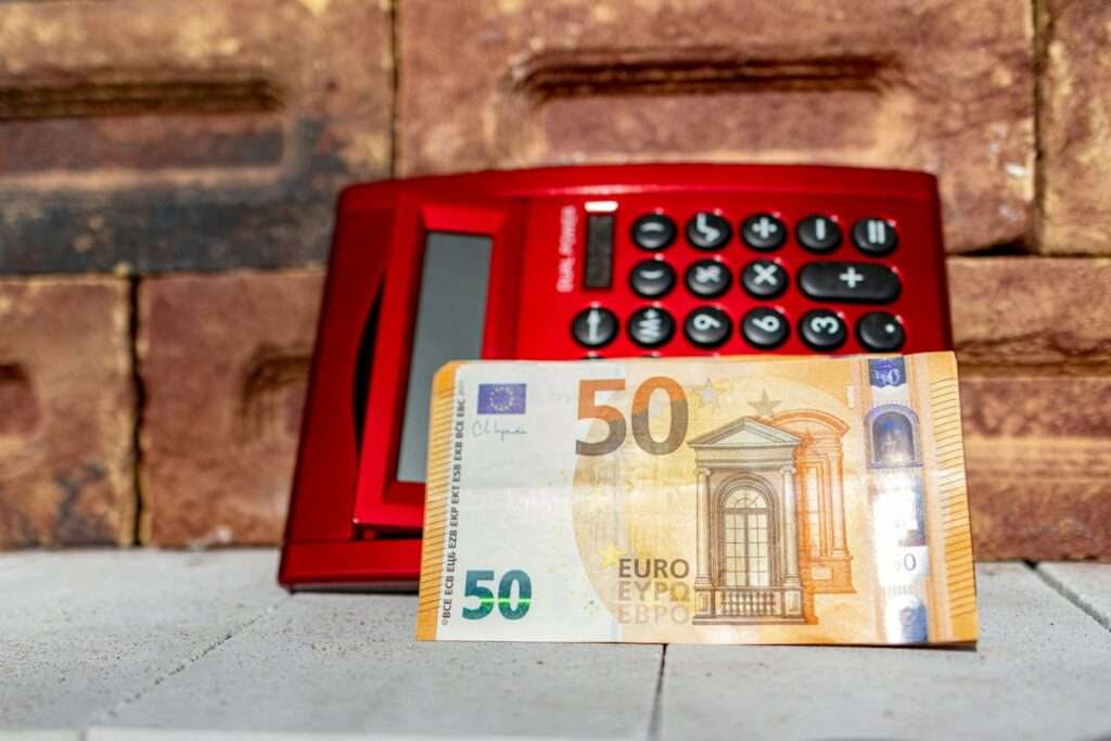 SEO Hannover - Ein roter elektronischer Rechner liegt auf einer Ziegeloberfläche, davor liegt ein 50-Euro-Schein. Die Szene vor einer Ziegelwand deutet subtil auf die Berechnung der Kosten für Website-Erstellung hin. Local SEO Agentur Hannover.