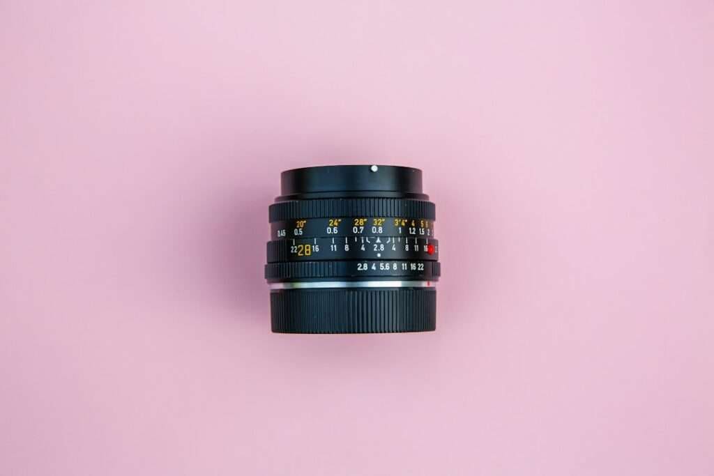 SEO Hannover - Dieses schwarze Kameraobjektiv mit seinem schlichten rosa Hintergrund ist für professionelle Fotografie konzipiert und verfügt über verschiedene Markierungen für Blenden- und Fokuseinstellungen. Der Blendenring zeigt Zahlen in Weiß und Gelb an und sorgt so für Präzision bei jeder Aufnahme. Local SEO Agentur Hannover.