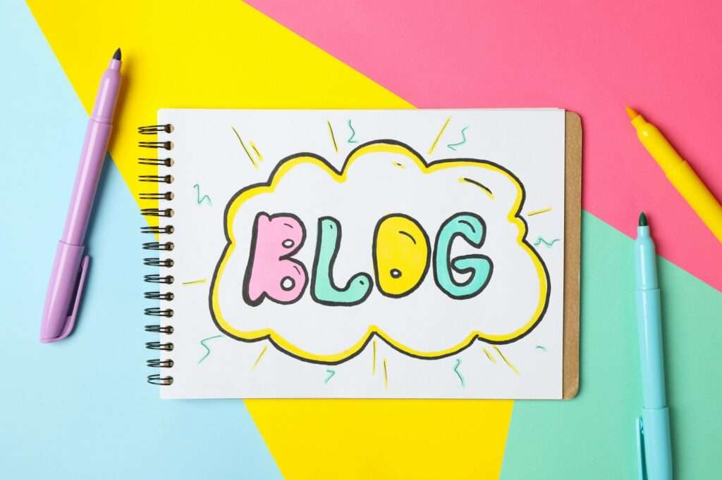 SEO Hannover - Ein Notizbuch mit der Aufschrift „BLOG“ in bunten Blasenbuchstaben auf einer weißen Seite liegt zwischen vier pastellfarbenen Markern in Lila, Blau, Gelb und Pink. Der Hintergrund zeigt ein geometrisches Design in Pink, Gelb und Blau – die perfekte Inspiration für die Gestaltung des Blog-Inhalts Ihrer Website. Local SEO Agentur Hannover.