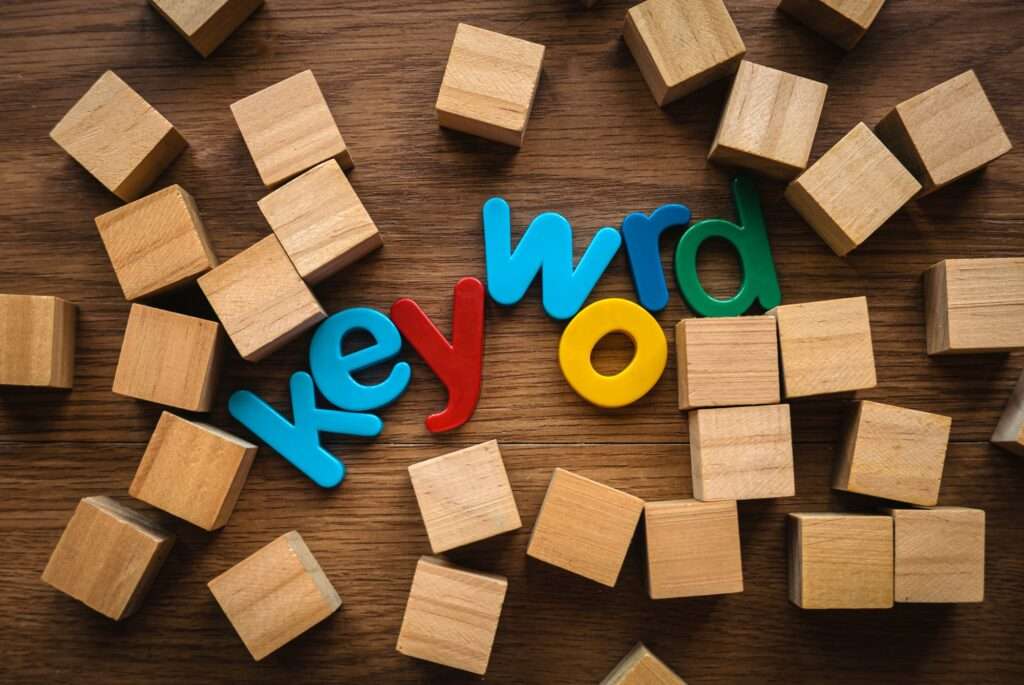Webdesign Hannover - Bunte Plastikbuchstaben mit der Aufschrift „Wie viele Keywords sind sinnvoll?“ sind umgeben von verstreuten Holzklötzen auf einer Holzoberfläche. Local SEO Agentur Hannover.