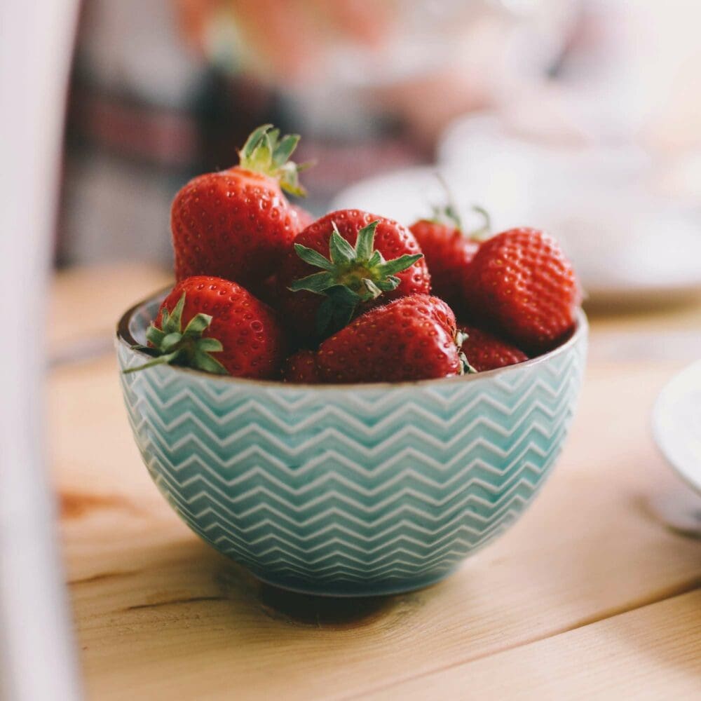 SEO Hannover - Eine türkisfarbene Schale mit Zickzack-Muster ist mit frischen Erdbeeren gefüllt und fängt die Essenz der Food Fotografie gekonnt ein. Die Schale ruht auf einer Holzoberfläche, während der Hintergrund kunstvoll unscharf bleibt. Local SEO Agentur Hannover.
