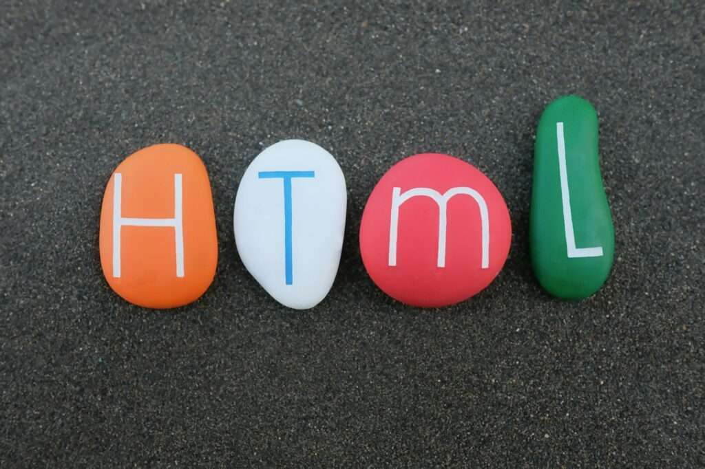 Webdesign Hannover - Vier farbige Steine mit den Buchstaben „H“, „T“, „M“ und „L“, die zusammen „HTML“ ergeben, liegen auf einem dunklen Sandgrund. Die Steine in leuchtenden Orange-, Weiß-, Rot- und Grüntönen ähneln den deutlichen Unterschieden zwischen einer XML-Sitemap und einer HTML-Sitemap bei der Führung digitaler Reisen. Local SEO Agentur Hannover.