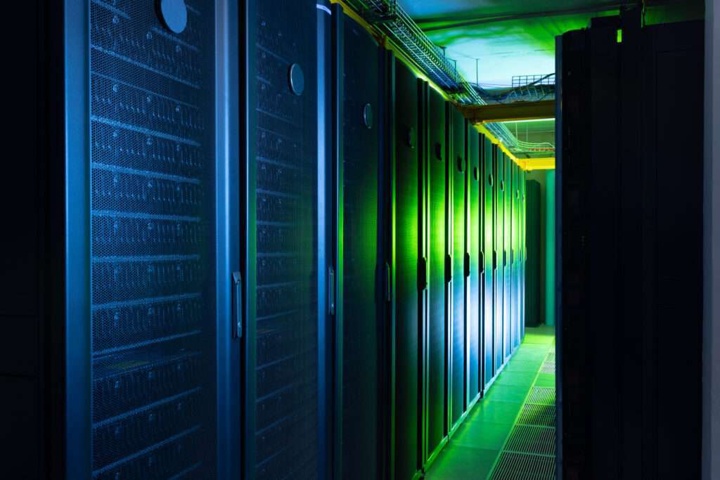 Webdesign Hannover - Ein schwach beleuchteter Serverraum mit Reihen hoher, schwarzer Server-Racks auf beiden Seiten, beleuchtet von grünen und blauen Lichtern, beherbergt die wichtige Datenbank bei einer Webseite. Durch die Mitte des Raumes führt ein schmaler Gang. Local SEO Agentur Hannover.