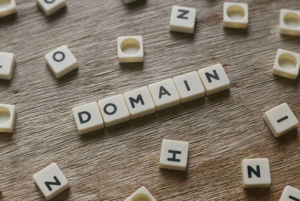 Webdesign Hannover - Scrabble-Steine mit der Schreibweise „DOMAIN“ sind auf einer Holzoberfläche angeordnet, umgeben von anderen verstreuten Steinen. Local SEO Agentur Hannover.