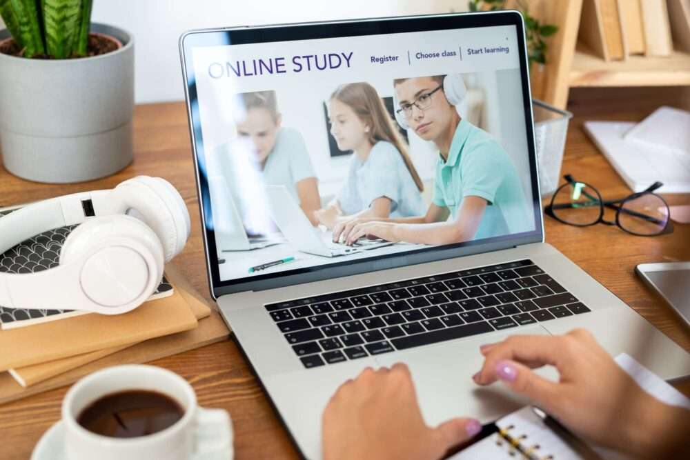Webdesign Hannover - Eine Person benutzt einen Laptop mit der Homepage „Online-Studium“. Studierende arbeiten fleißig. In der Nähe liegen wichtige Dinge wie Notizbuch, Stift, Kopfhörer, Kaffeetasse und Topfpflanze auf dem Holzschreibtisch. Auf dem Bildschirm steht „Online-Studium“ und bietet Baukasten-Optionen zur Anmeldung und Kurswahl. Local SEO Agentur Hannover.