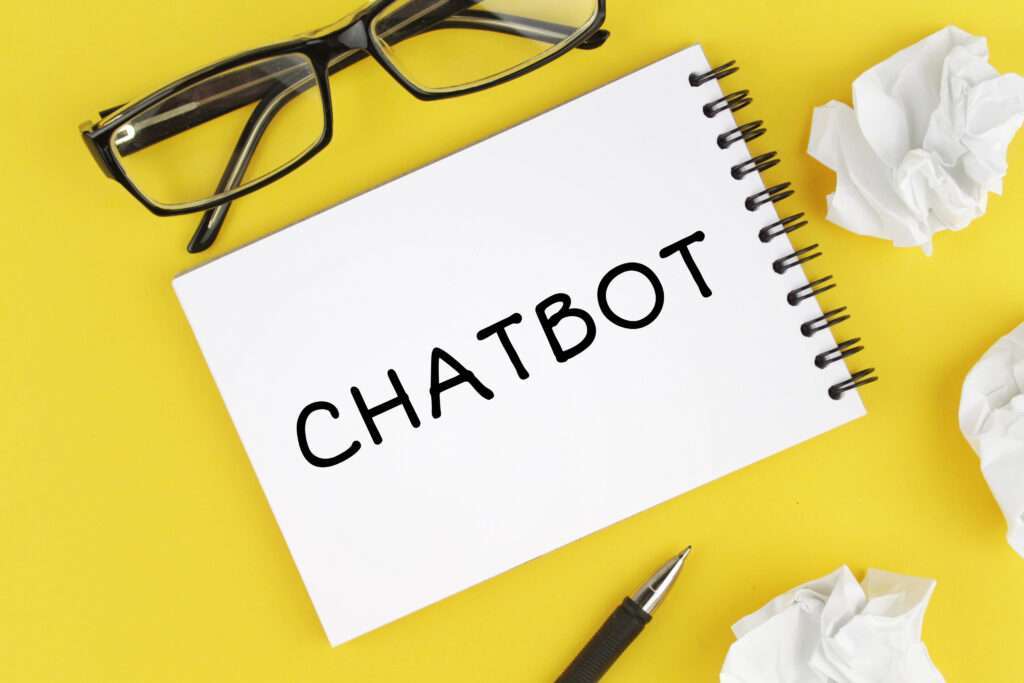 Webdesign Hannover - Eine Brille mit schwarzem Rahmen liegt über einem offenen Notizbuch mit der Aufschrift „Wie implementiere ich einen Chatbot?“. Das Notizbuch liegt auf gelbem Hintergrund, umgeben von einem schwarzen Stift und zerknüllten Papierkugeln. Local SEO Agentur Hannover.