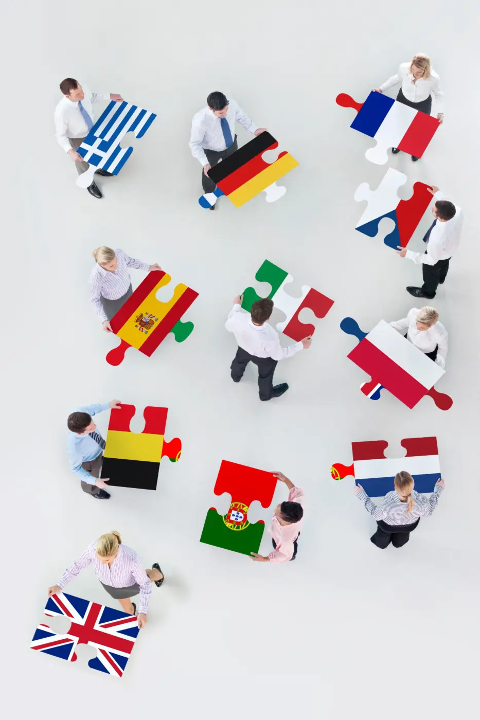 Webdesign Hannover - Neun Personen, die auf einem weißen Boden stehen, halten große Puzzleteile mit verschiedenen europäischen Nationalflaggen in den Händen – darunter Großbritannien, Deutschland, Frankreich, Spanien, Italien, Portugal, Griechenland, die Niederlande und Belgien –, die die mehrsprachige Einheit symbolisieren, ähnlich wie WPML WordPress eine nahtlose Sprachintegration auf europäischen Websites ermöglicht. Local SEO Agentur Hannover.